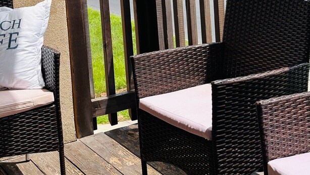 Un balcon avec des fauteuils en osier et, en arrière-plan, un bâtiment blanc.