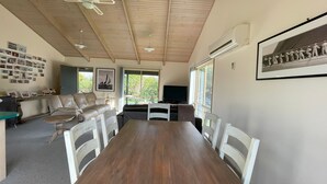 Un salón con una mesa de comedor de madera, sillas blancas, un sofá de cuero, un televisor y un ventilador de techo.