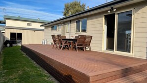 Una terraza de madera con una mesa, sillas, una puerta corrediza de vidrio y un porche cubierto.