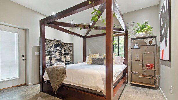 Una cama con dosel y cuatro columnas que ofrece vistas de un paisaje urbano a través de la ventana.