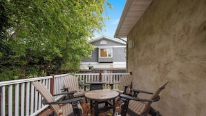 Un patio al aire libre con terraza de madera, una mesa y cuatro sillas Adirondack.