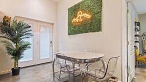 Un comedor moderno con una mesa redonda y sillas traslúcidas, una planta en maceta y una obra de arte de neón en la pared.