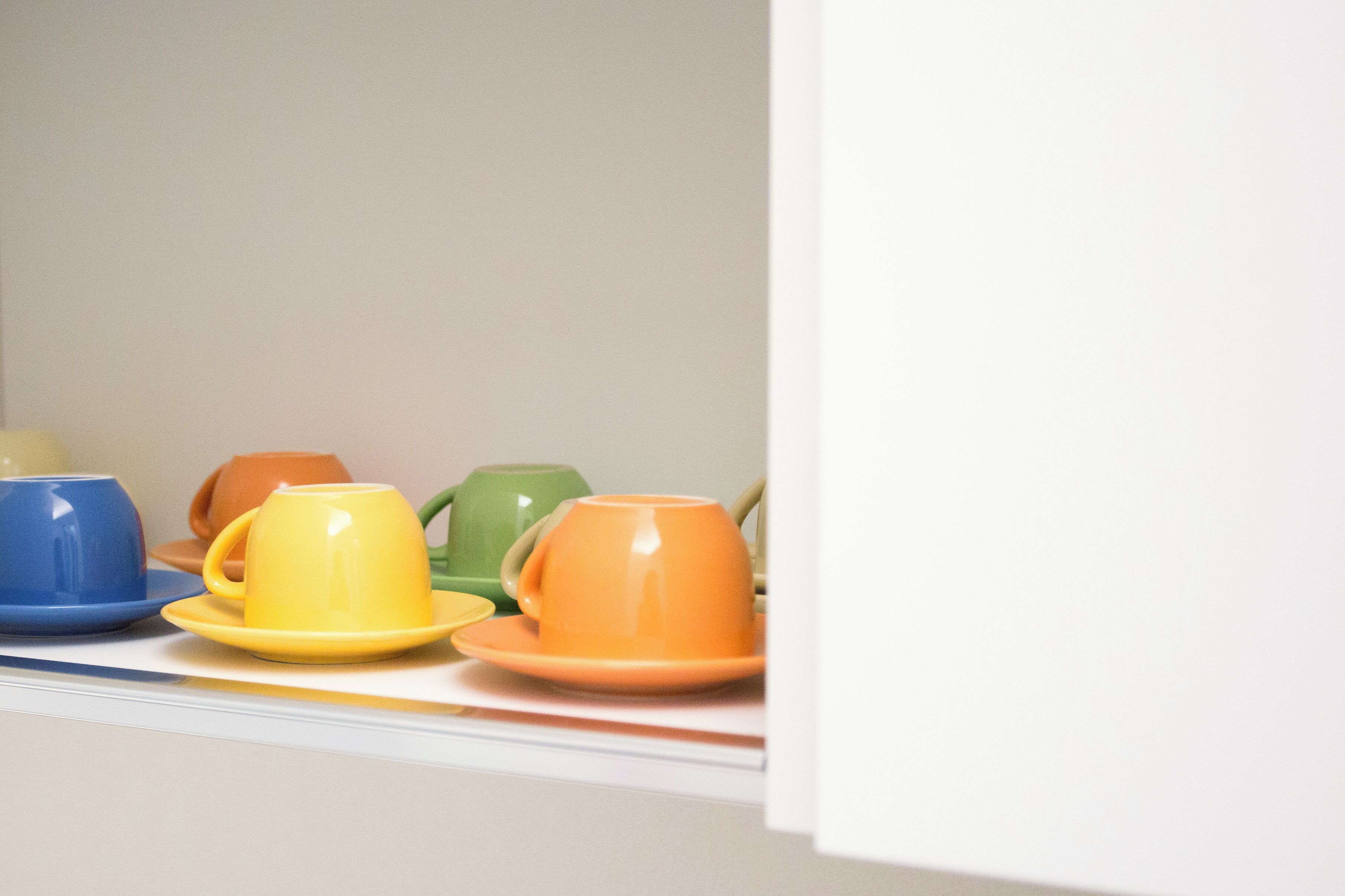 A row of colorful cups and saucers on a shelf.