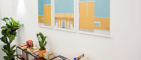 A wall with three framed pictures of a building with the sign 'CINECITTA'. There are books on a shelf and two potted plants.