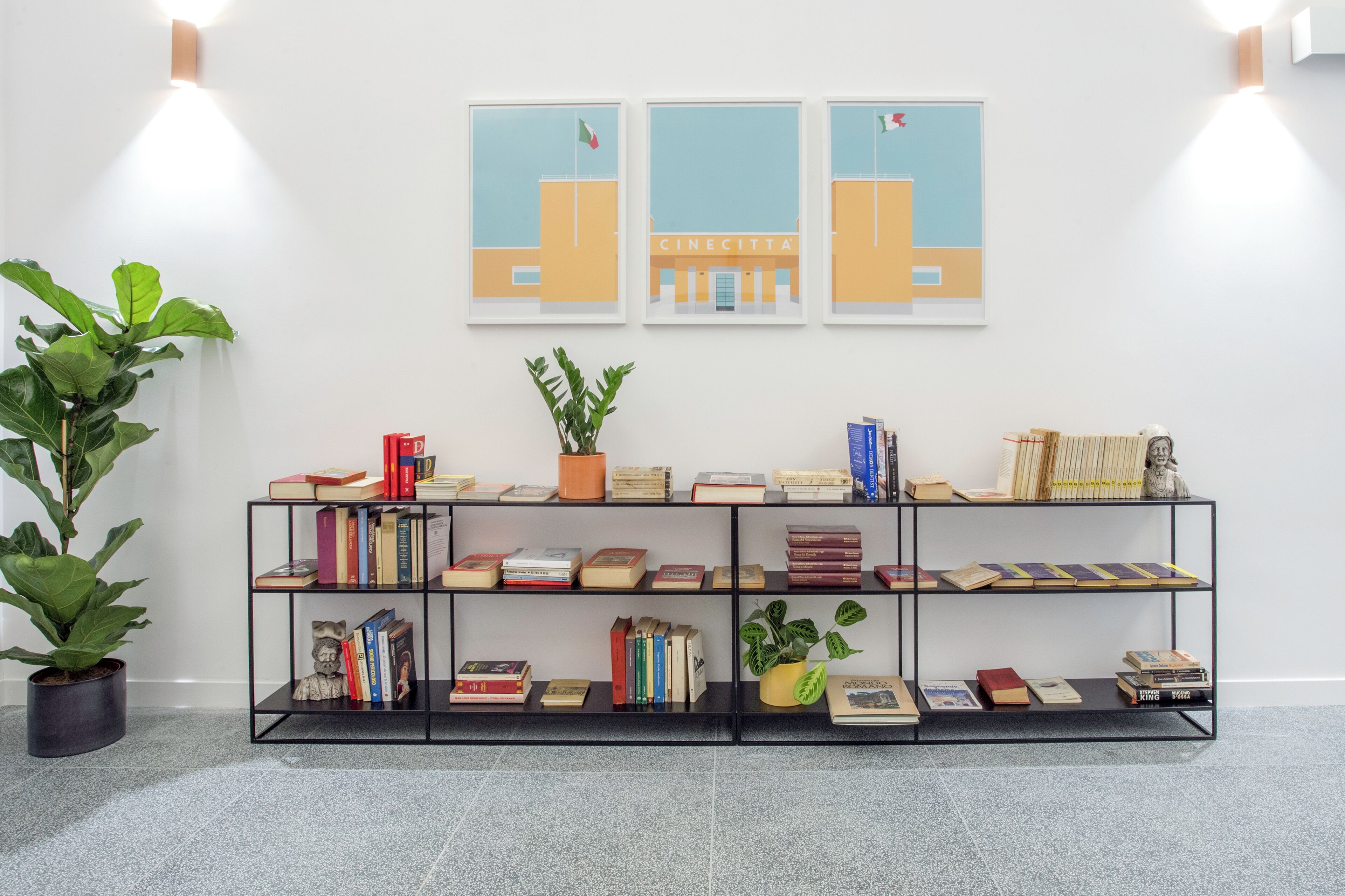 Une bibliothèque remplie de livres et d’objets décoratifs, une plante en pot et des œuvres d’art encadrées accrochées au mur.