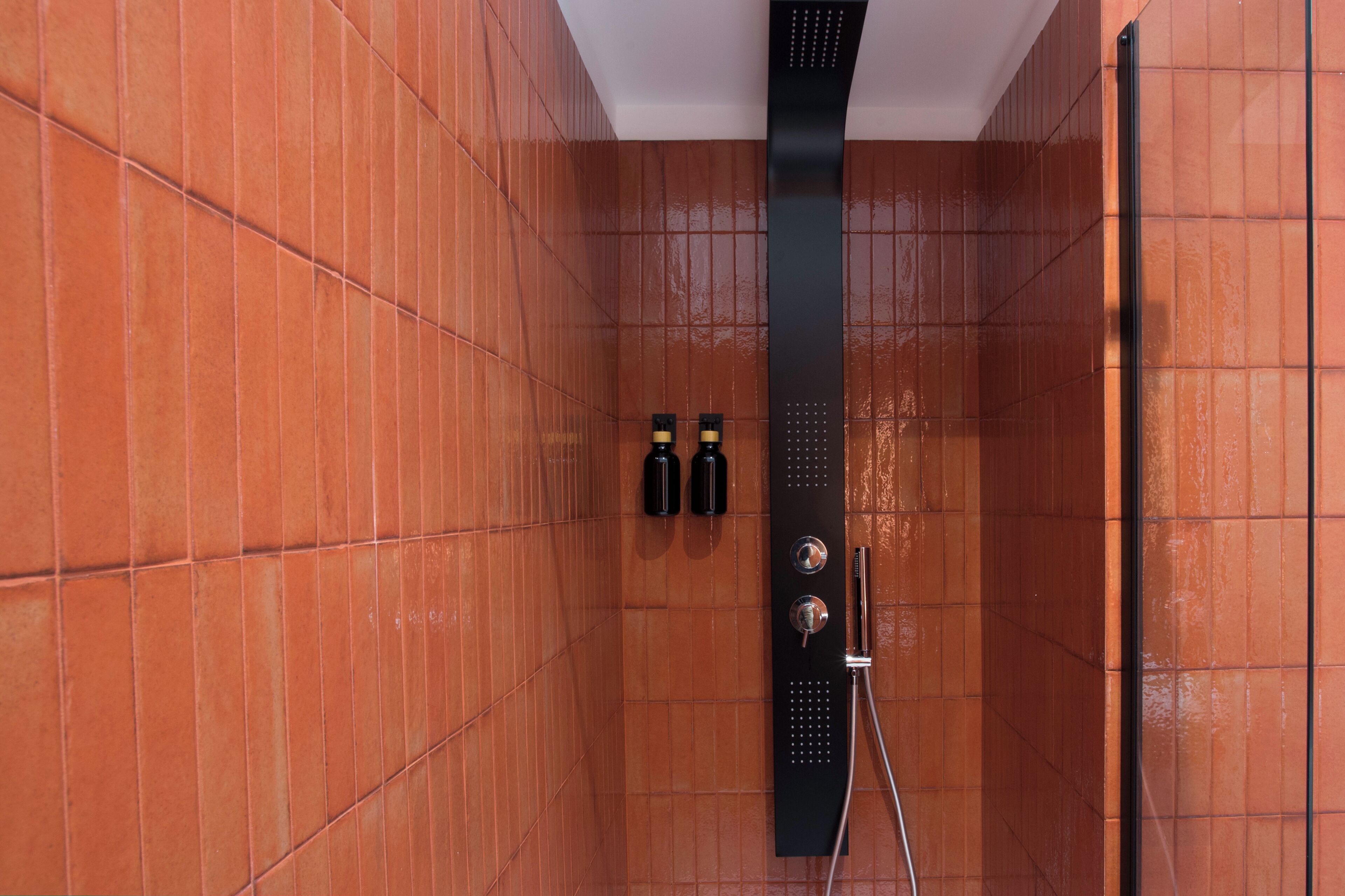 A shower area with tiled walls and a black shower panel.