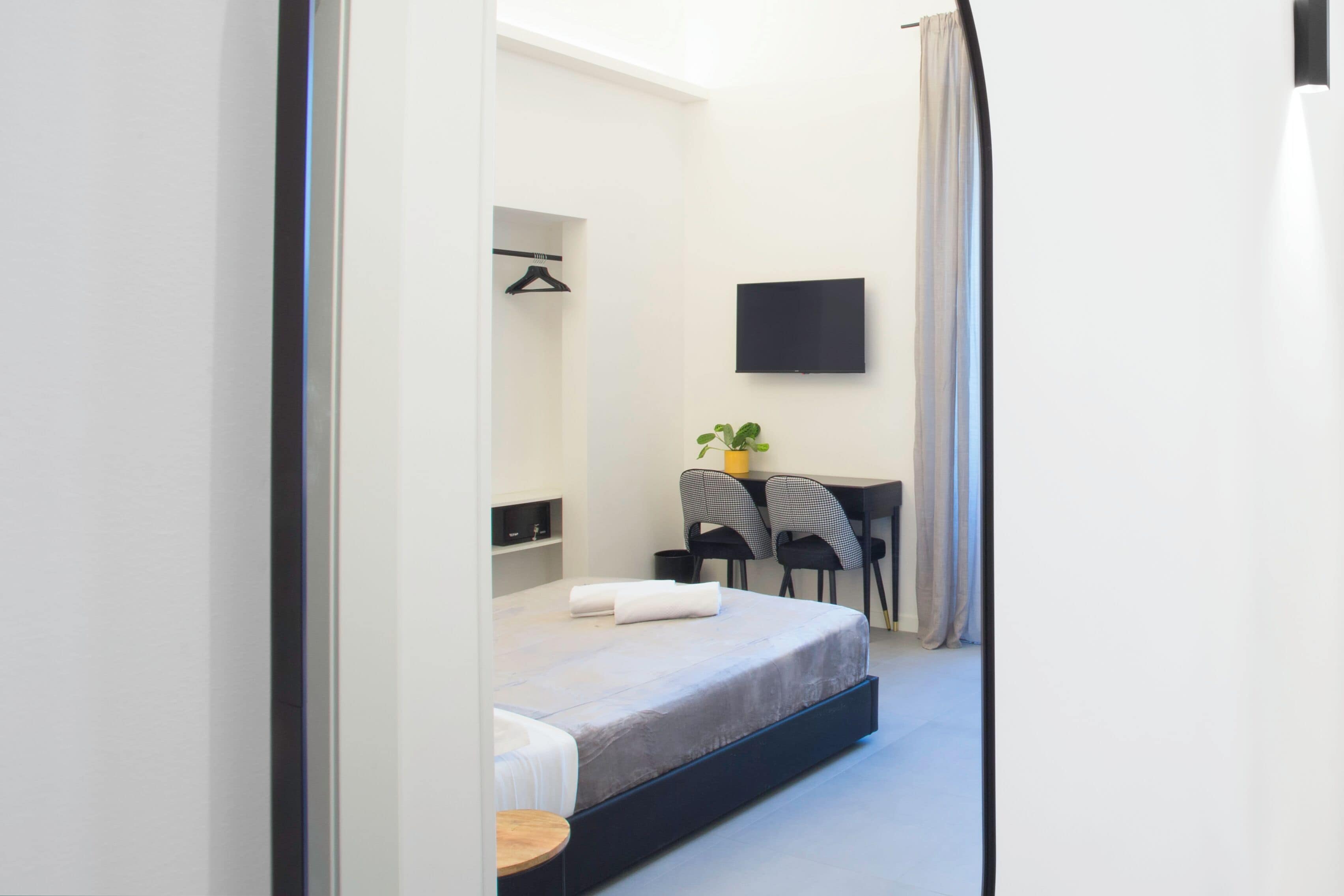 Un dormitorio moderno con cama, escritorio y silla. Hay un televisor en la pared y una planta en el escritorio.