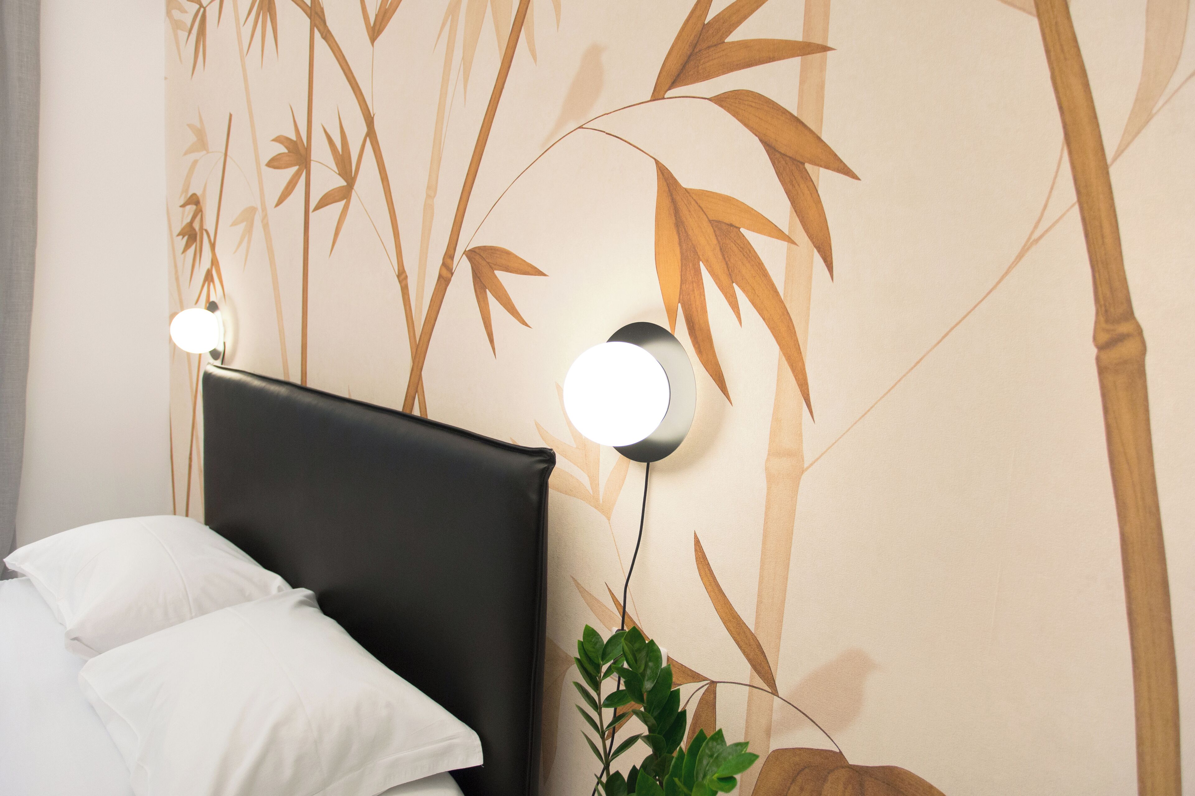A hotel room with a bed, a headboard, and wall-mounted lights.