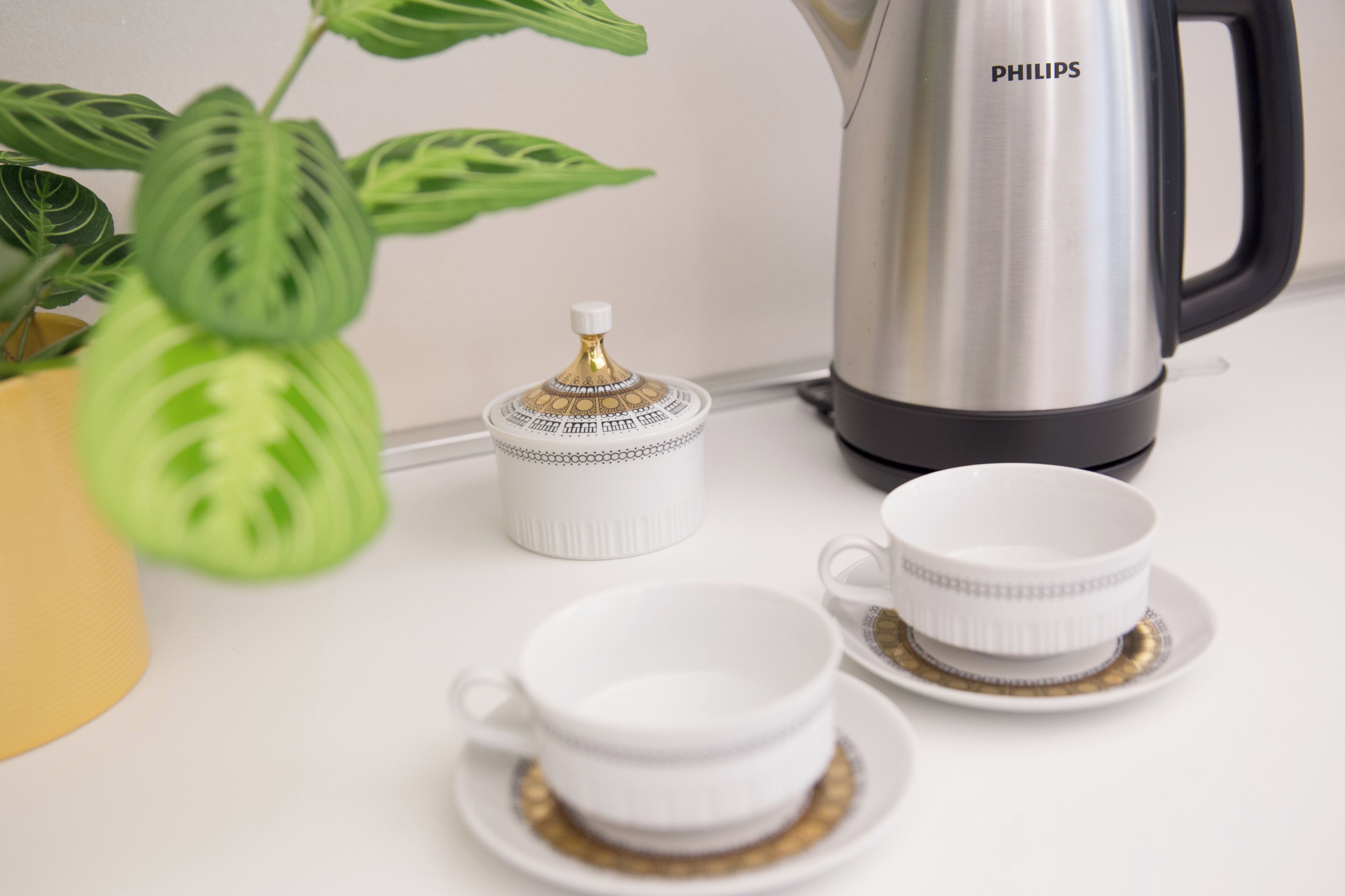 Un plan de travail de cuisine avec une machine à café, un petit pot blanc avec un couvercle et deux tasses blanches avec leurs soucoupes.