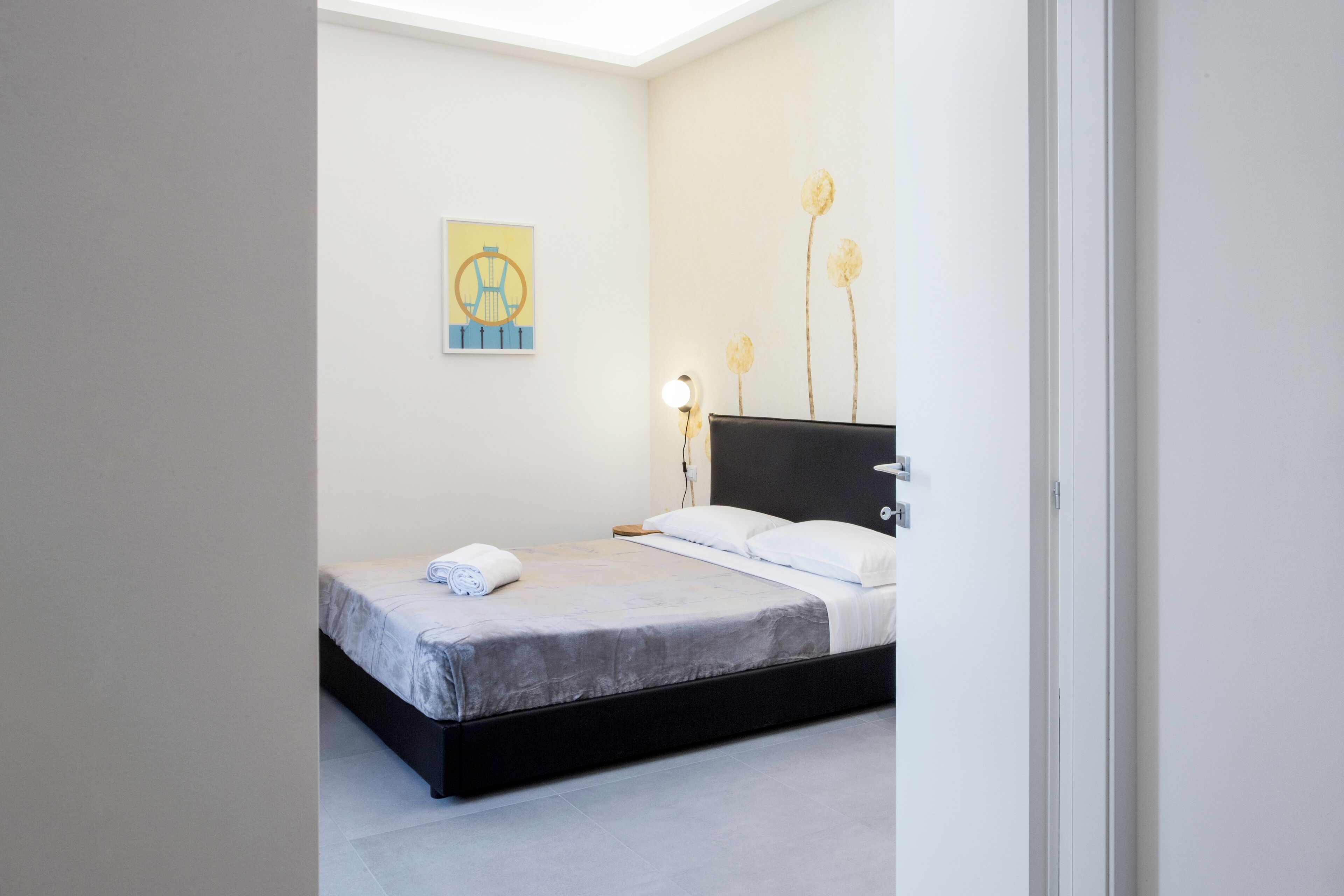 A neatly made bed with a grey and white duvet, a bedside lamp, and a wall-mounted artwork.