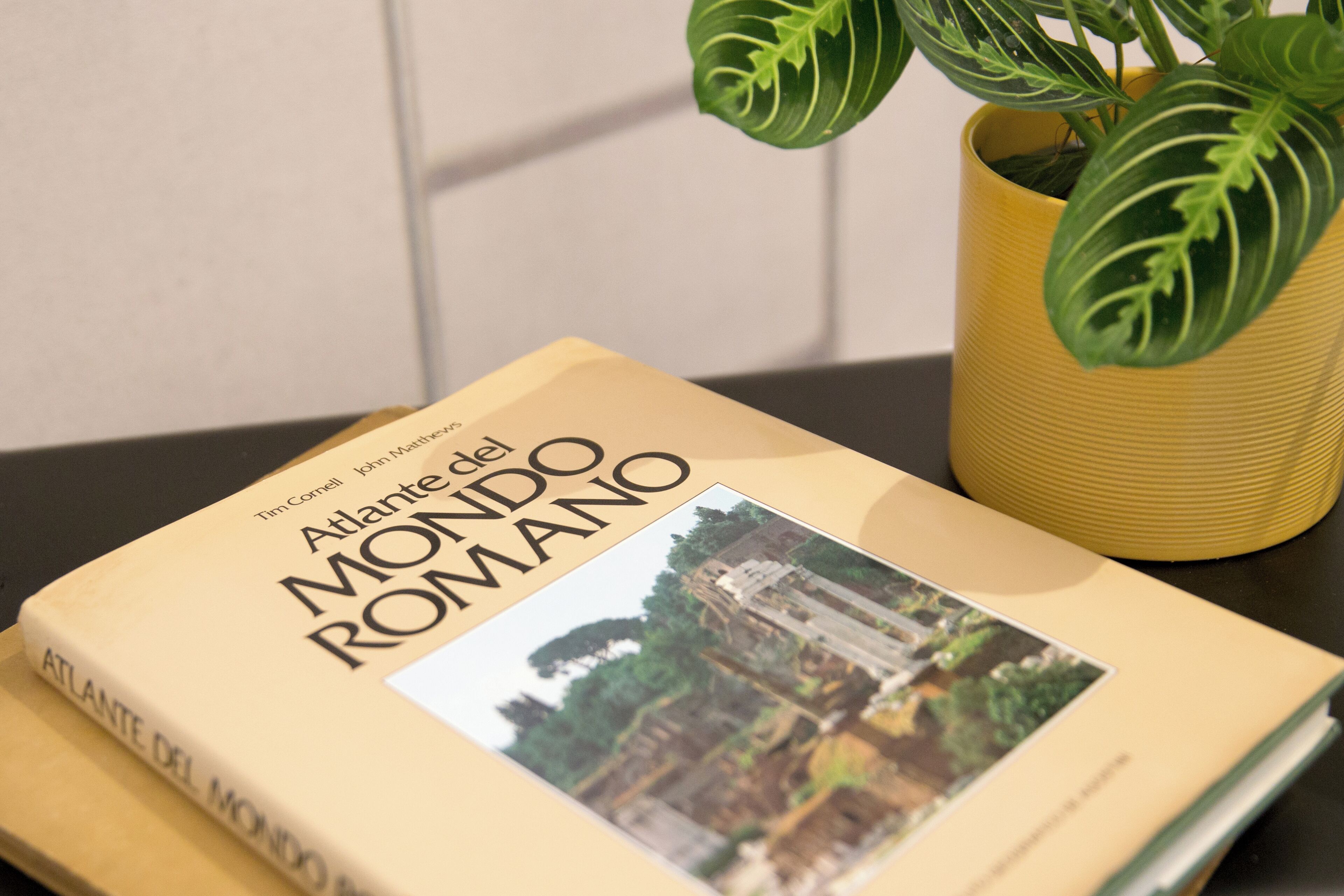 A book titled "Atlante del Mondo Romano" by Tim Cornell, placed on a surface next to a yellow pot with green leaves.