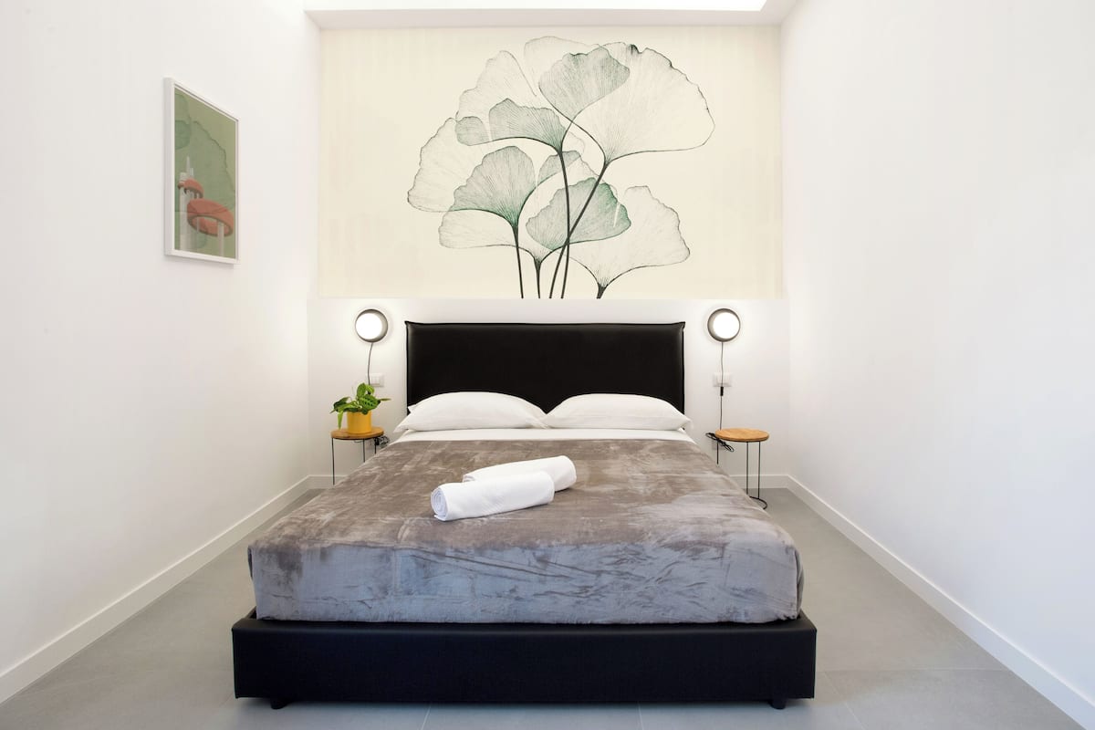 Une chambre moderne avec un grand lit, une œuvre d’art accrochée au mur, des tables de chevet et une plante en pot.