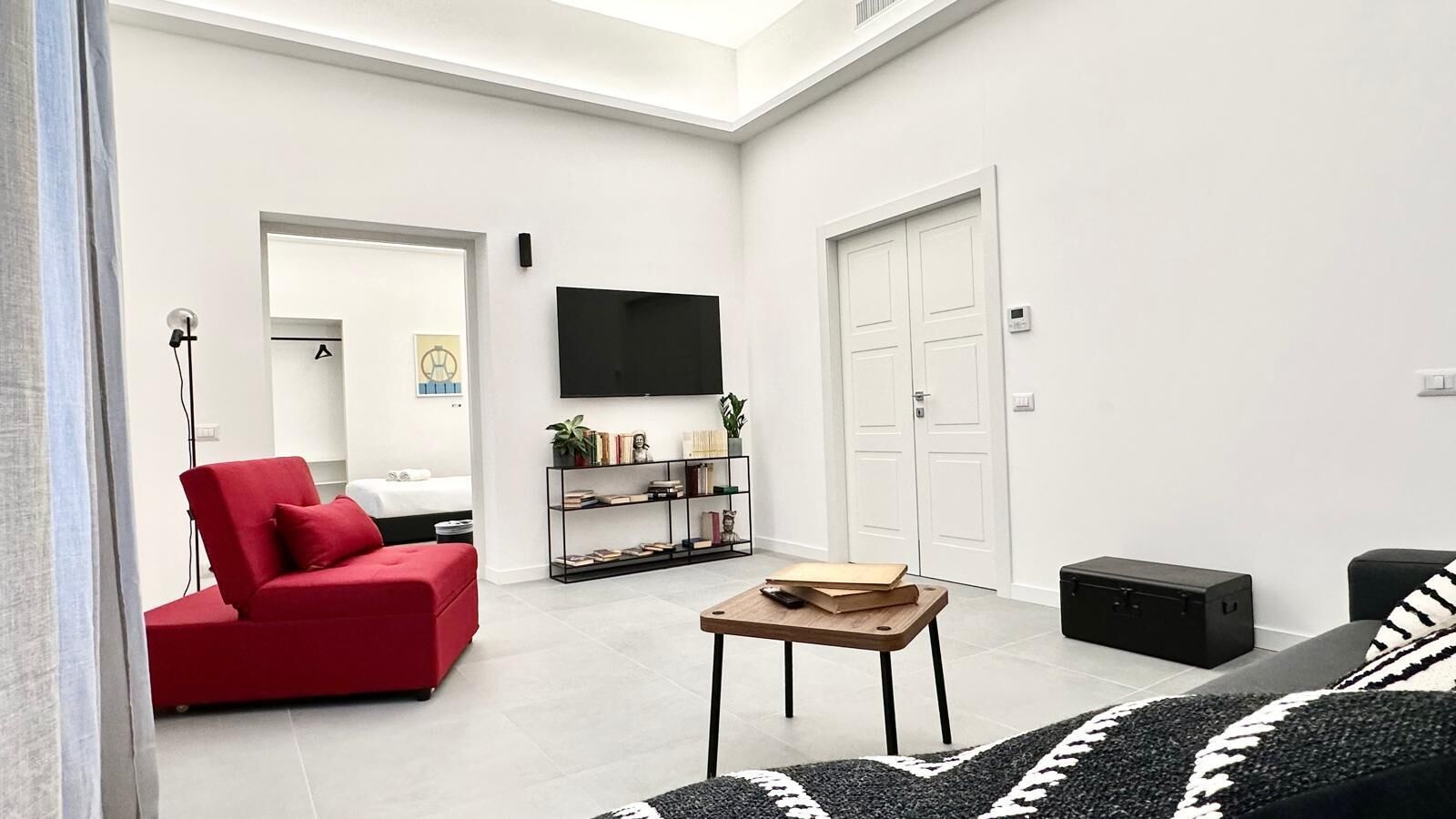 Un salon moderne avec un canapé rouge, une table basse en bois, un téléviseur fixé au mur et une bibliothèque.