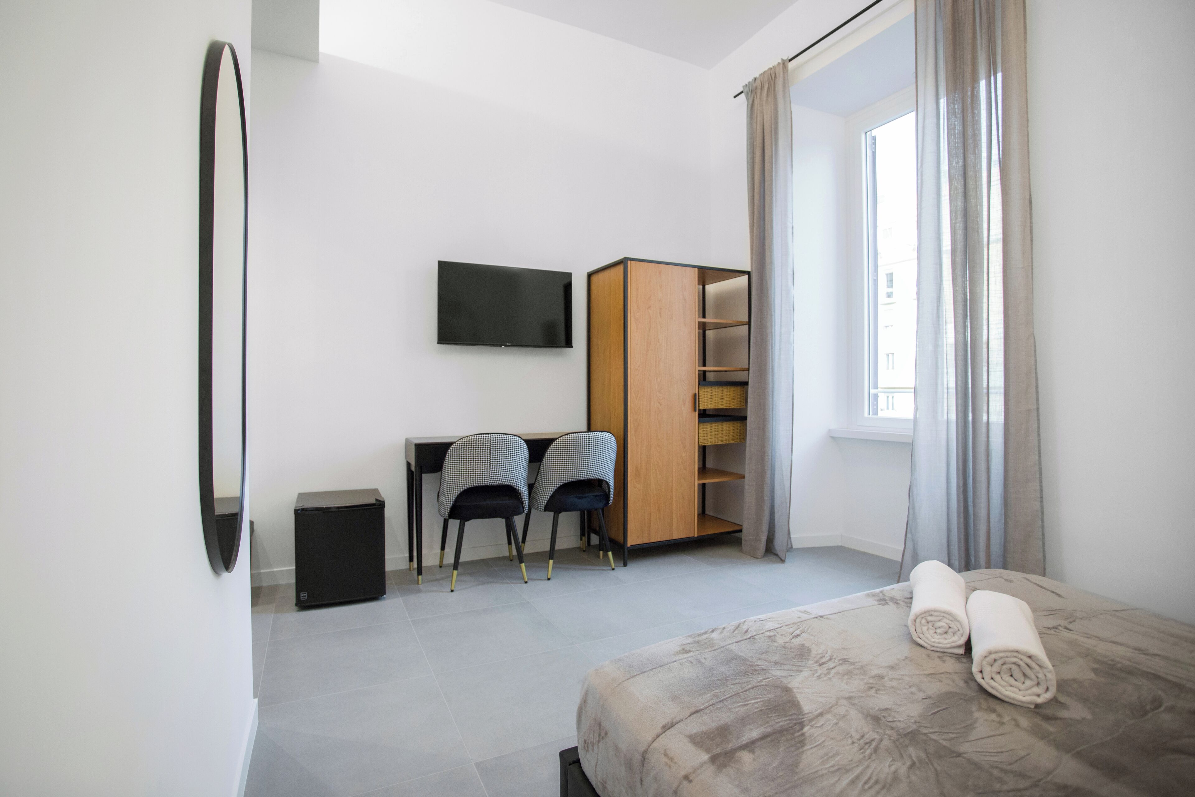 A modern bedroom with a bed, a TV, a desk, two chairs, and a wardrobe.