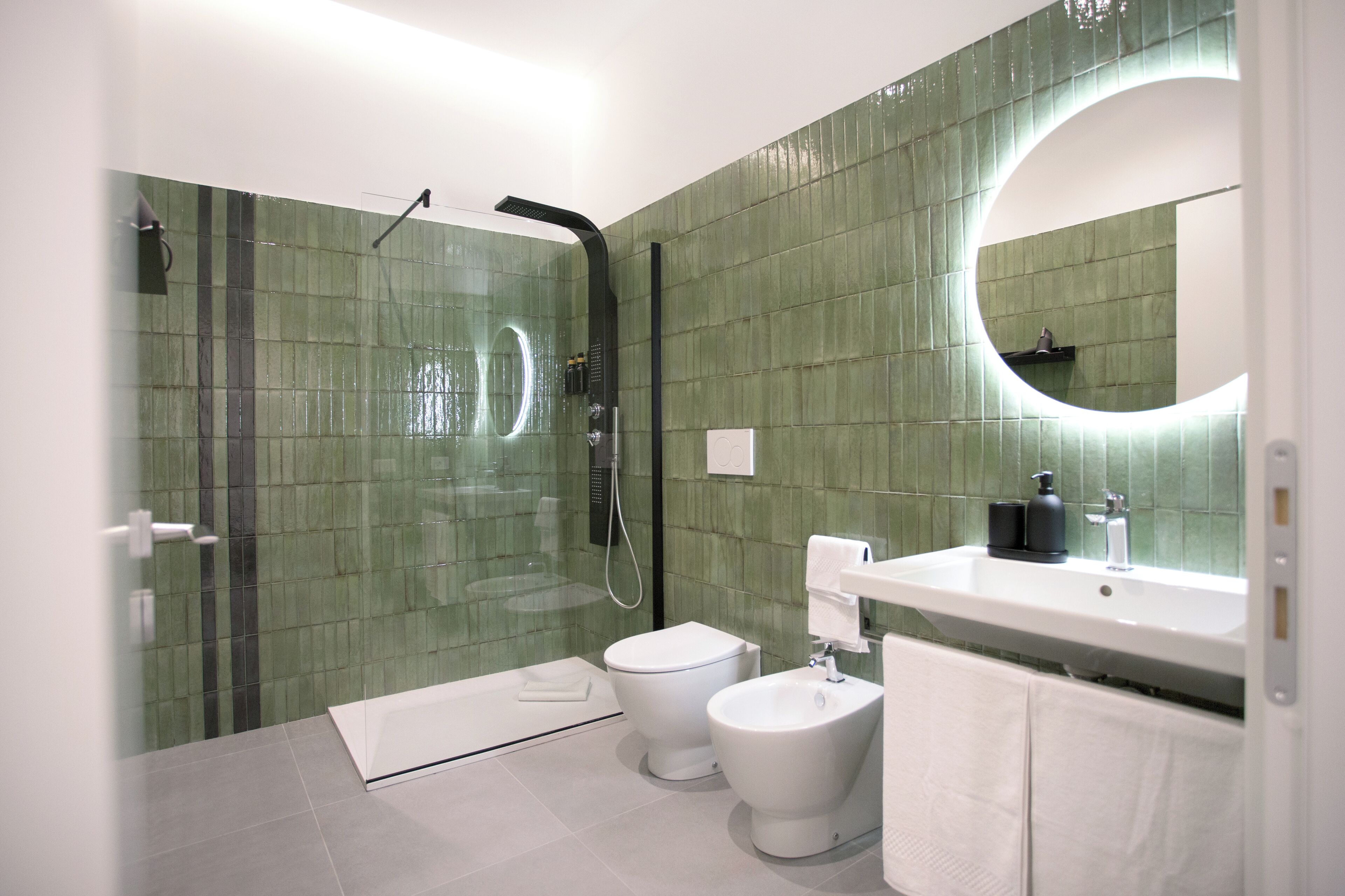 A modern bathroom with a glass-enclosed shower, a white toilet, a bidet, and a sink with a mirror above it.