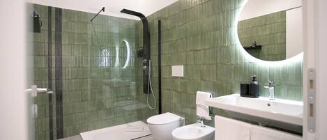 A modern bathroom with a glass-enclosed shower, a white toilet, a bidet, and a sink with a mirror above it.