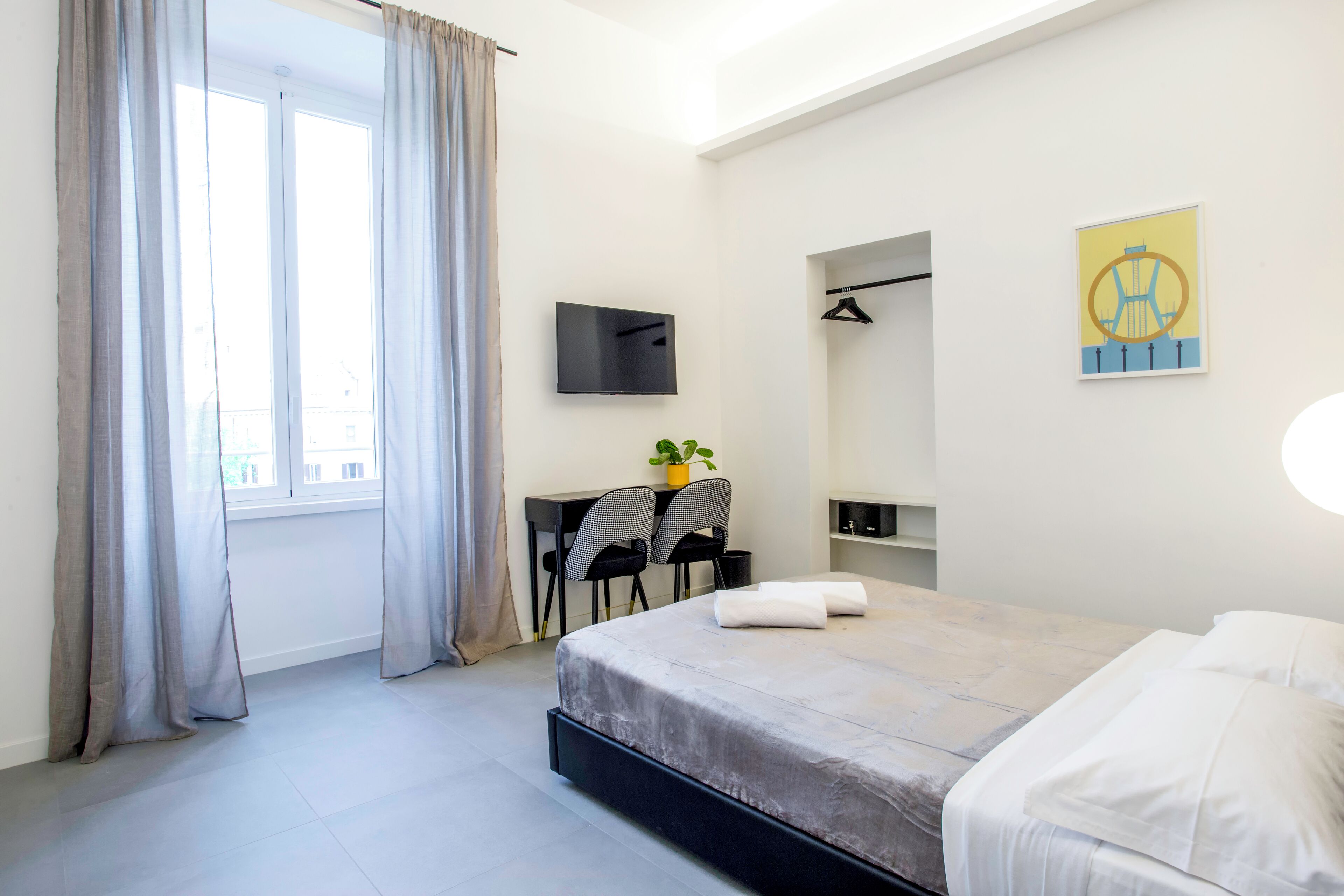 A modern hotel room with a bed, a desk with two chairs, a TV, and a painting on the wall.