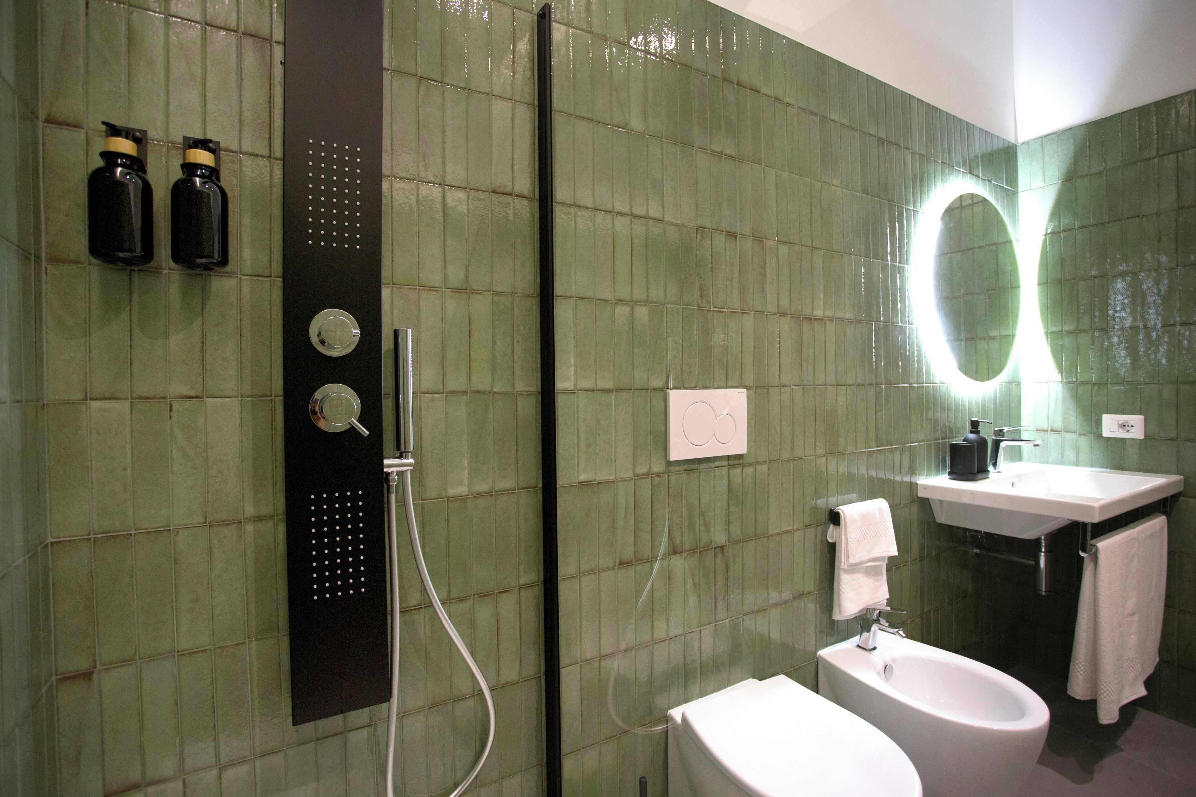 Un baño con pared de azulejos verdes, ducha, lavamanos y bidé.