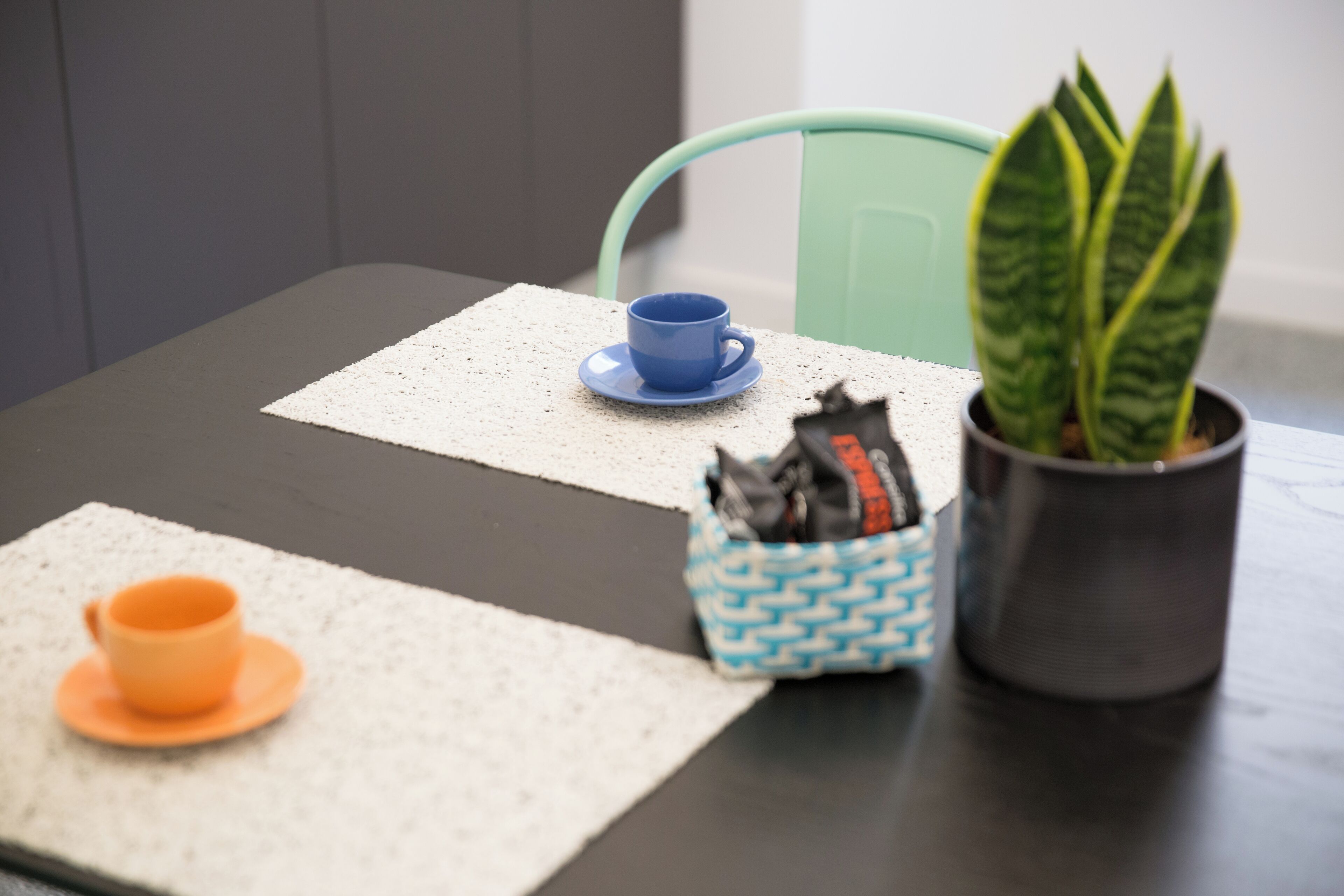 A table with a blue cup, a green chair, and a potted plant.