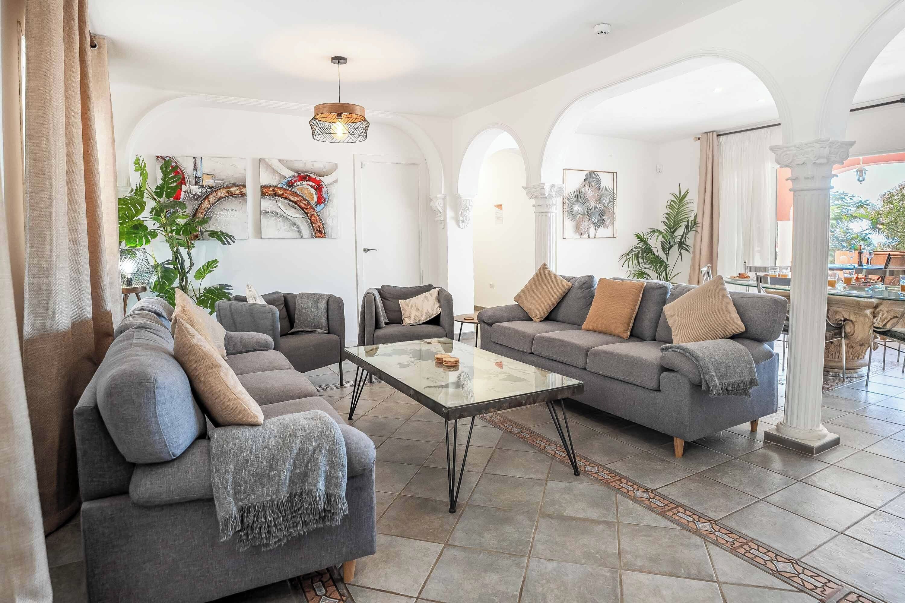 Un espacio habitable amplio con dos sofás grises, una mesa de centro de vidrio y vistas al patio exterior.