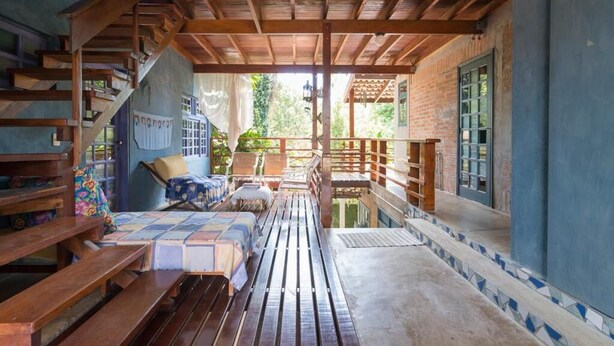 A covered outdoor seating area with wooden benches and a sofa, a staircase, and a view of greenery. - Pousada Mandala Maresias (São Sebastião)