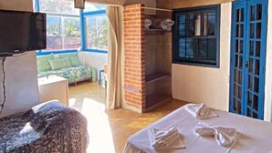 A room with a bed, a TV, a brick fireplace, and a window with blue shutters. - Pousada Mandala Maresias (São Sebastião)