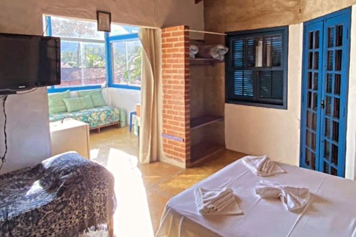 Una habitación con cama, televisión, chimenea de ladrillo y ventana con contraventanas azules.