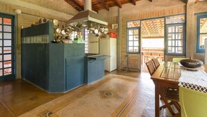 A kitchen with a central island, a dining area with a table and chairs, and a view through a window with a wooden lattice. - Pousada Mandala Maresias (São Sebastião)