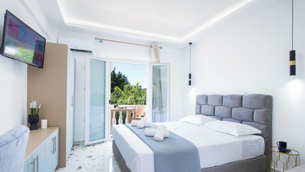 Une chambre moderne avec un grand lit, un téléviseur fixé au mur, un balcon donnant sur un espace verdoyant et une petite table avec une tasse.