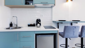 Une cuisine moderne avec des armoires de couleur turquoise, un évier en acier inoxydable, une machine à café et un lave-vaisselle. On y trouve deux tabourets de bar et un luminaire suspendu au-dessus du comptoir.