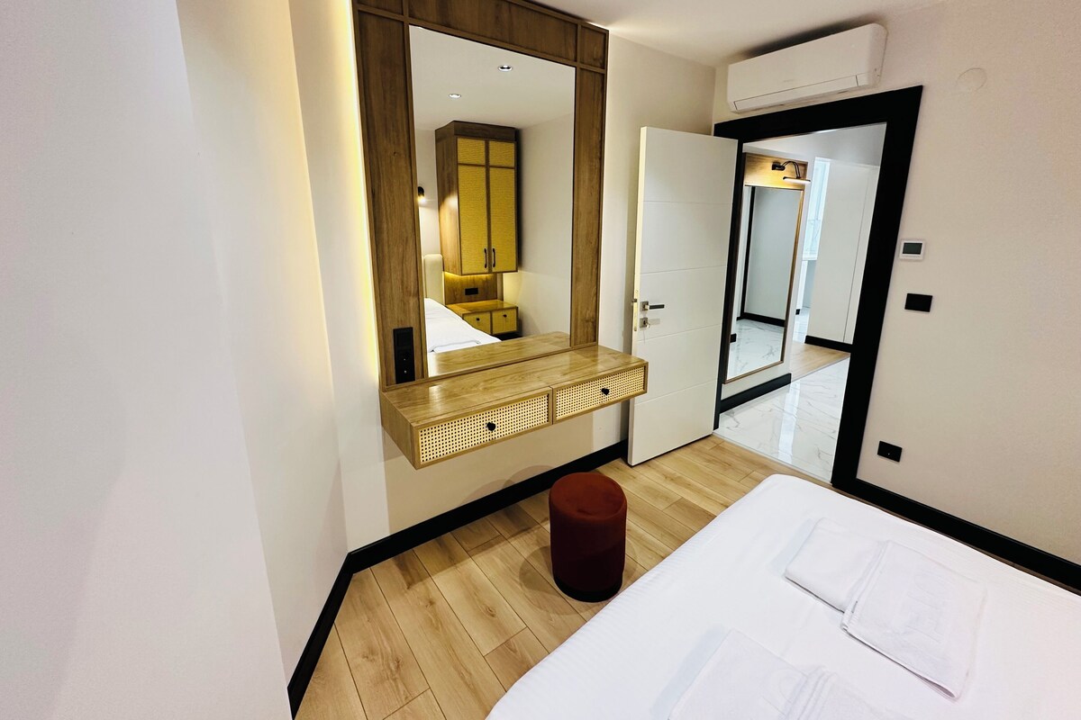 A modern hotel room with a large mirror, wooden wardrobe, and a bedside table.