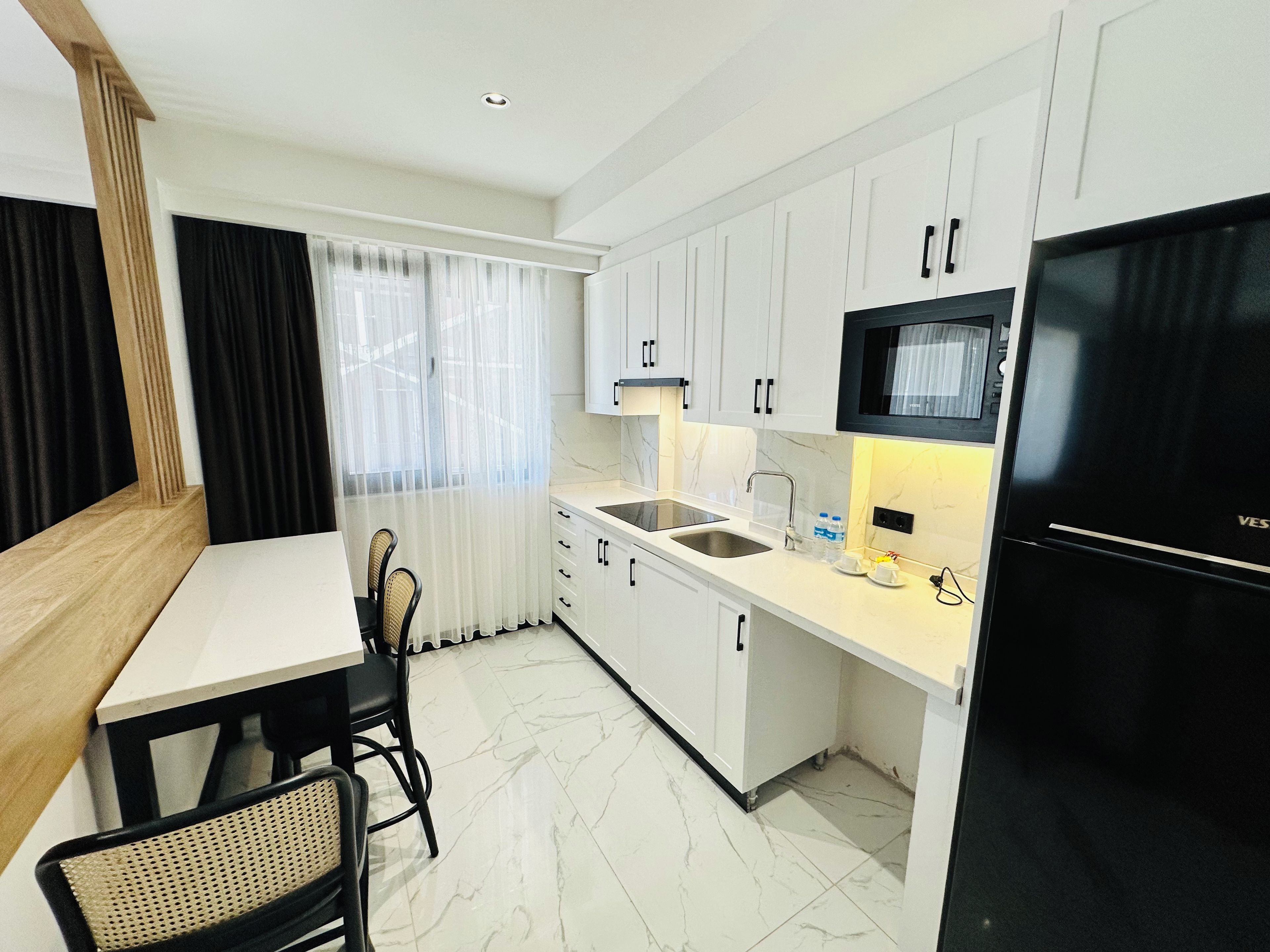 A modern kitchen with white cabinetry, a black refrigerator, and a dining area with a table and chairs.