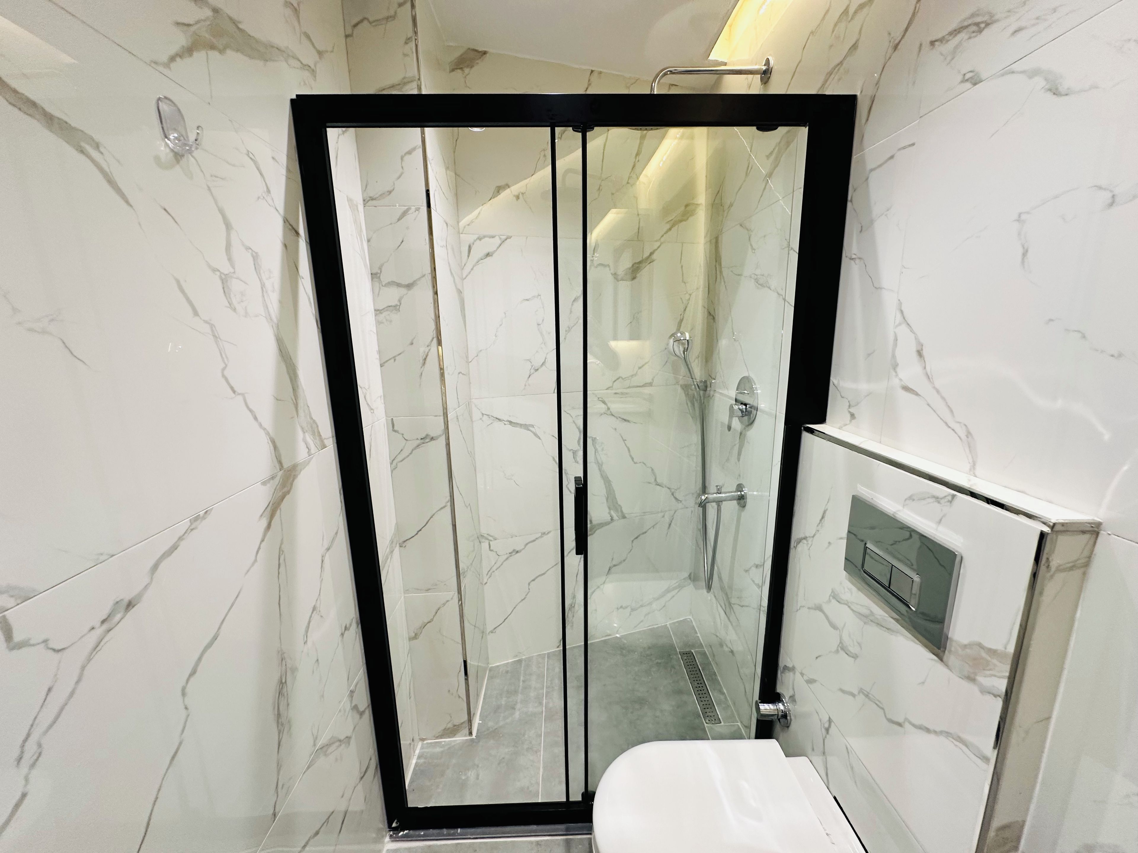 A modern bathroom with a glass-enclosed shower, marble walls, and a toilet with a control panel.