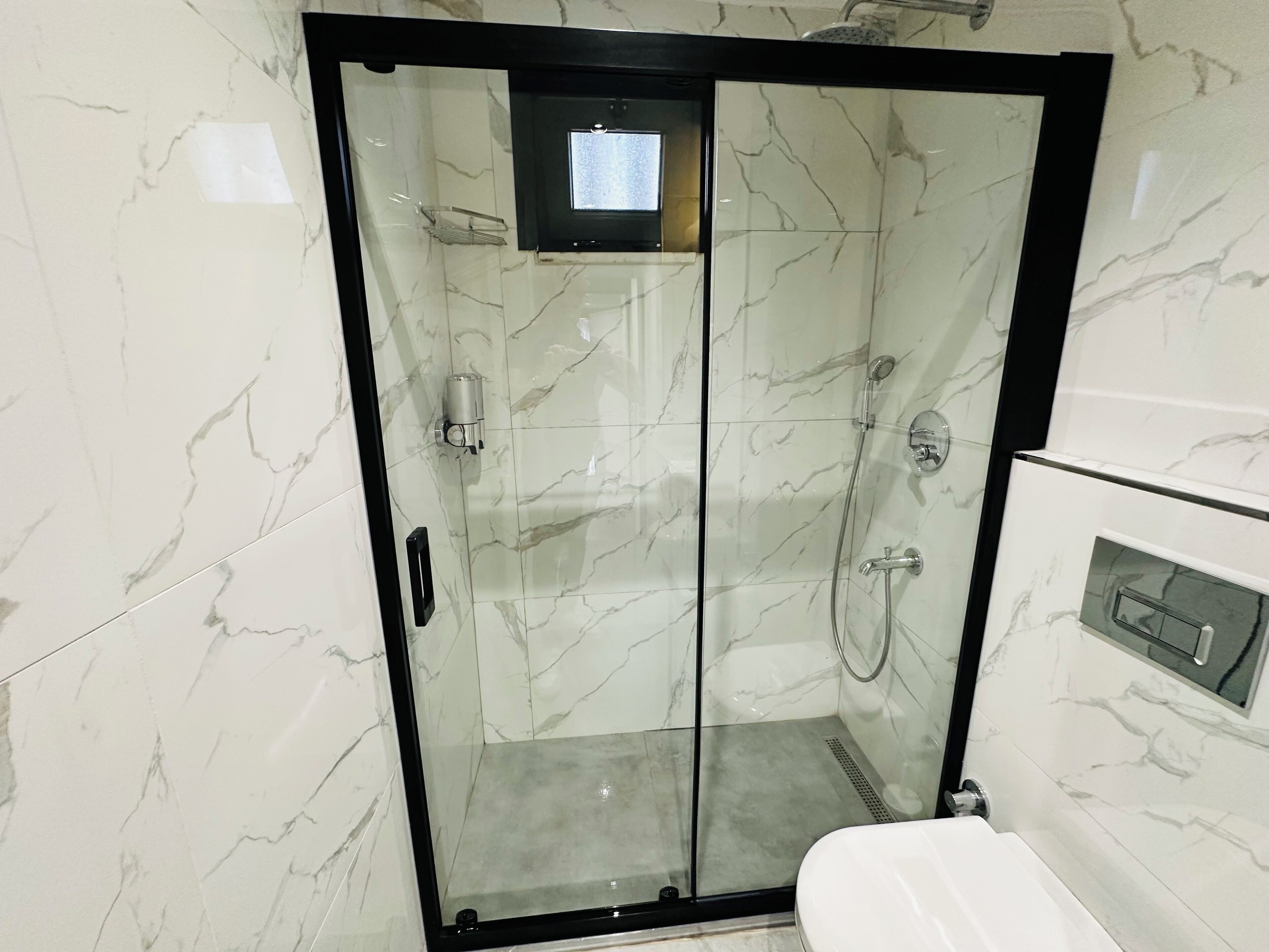 A glass-enclosed shower stall with a handheld showerhead and a handheld faucet.