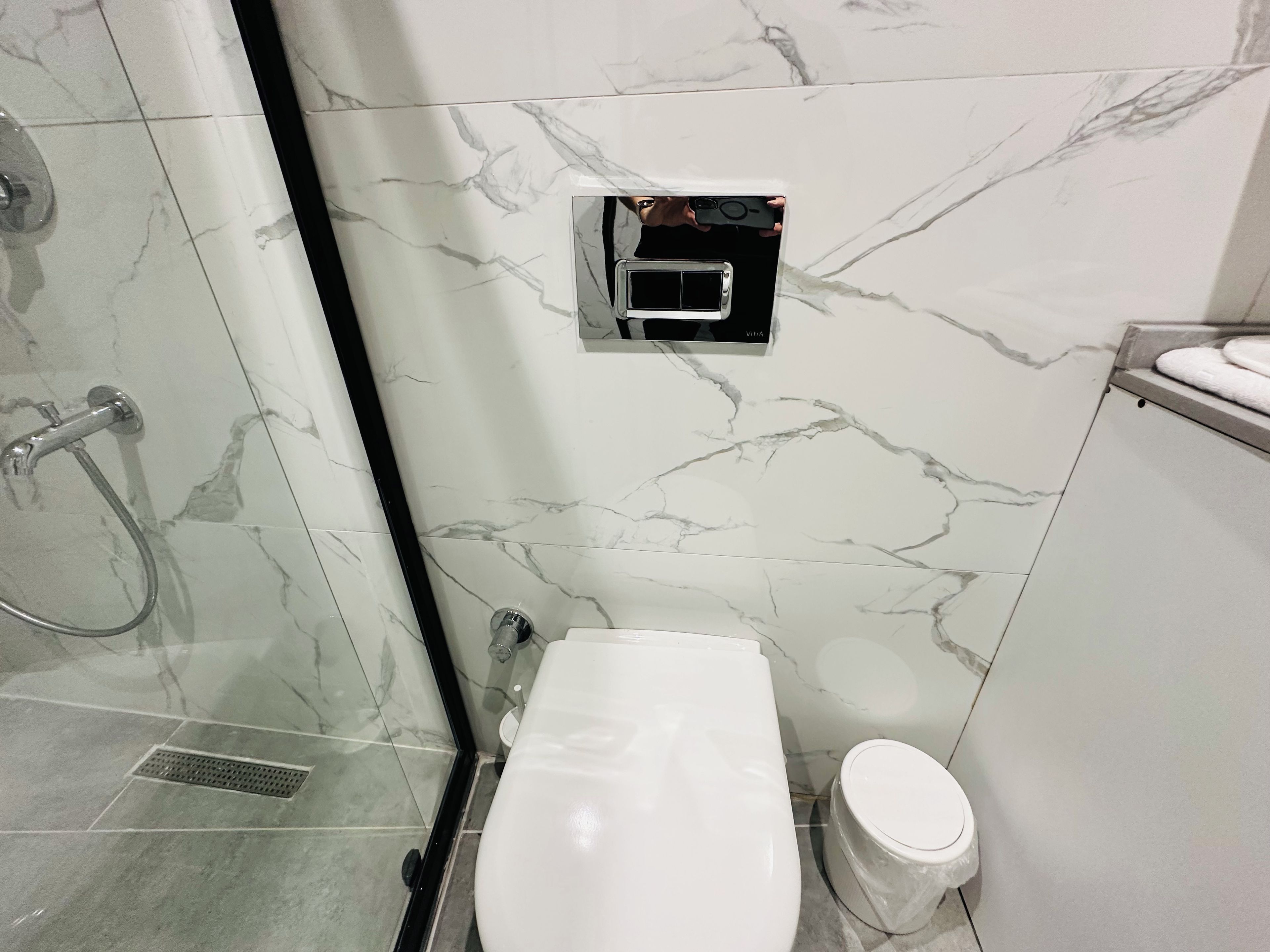 Un baño con inodoro, ducha y pared de mármol.