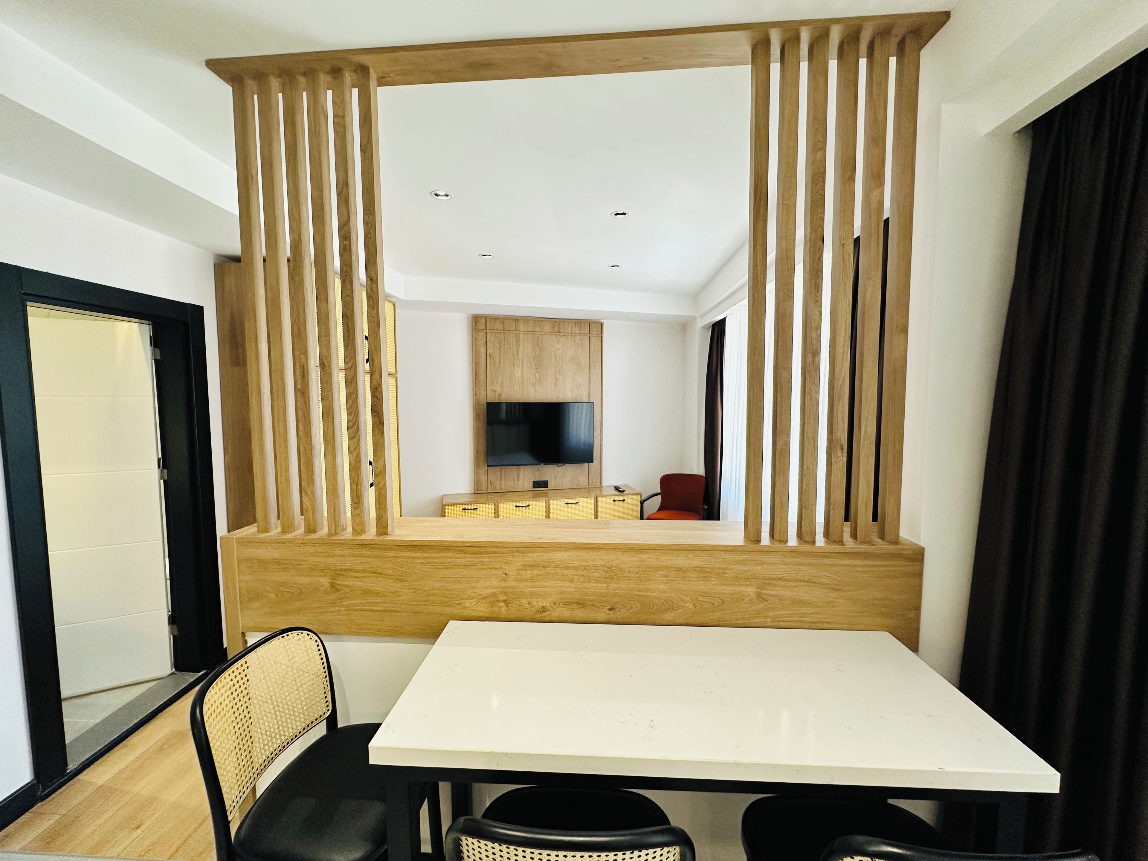 A modern hotel room with a dining area, a TV mounted on the wall, and a wooden partition.