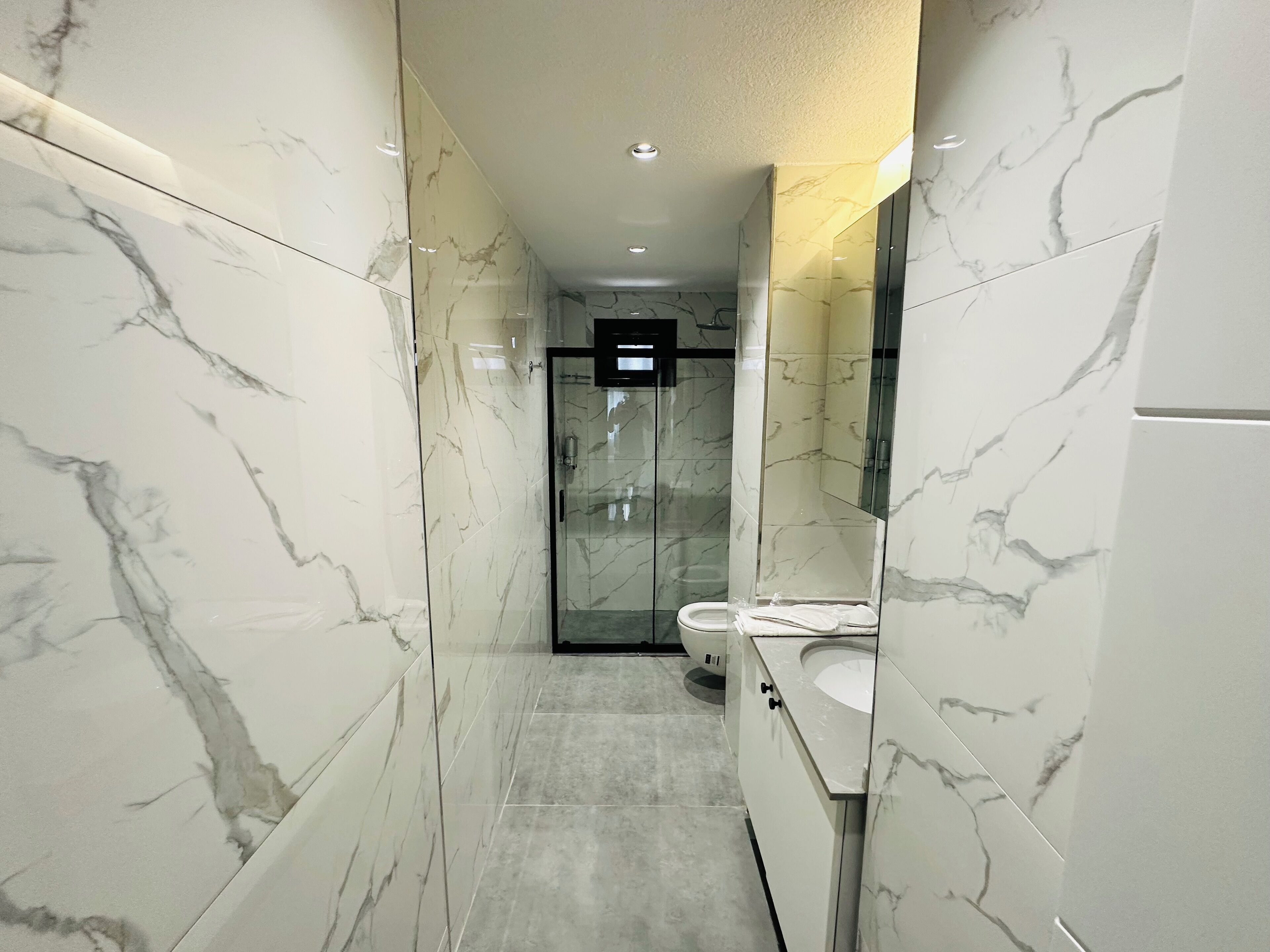 A modern bathroom with marble walls, a glass shower enclosure, and a white sink.