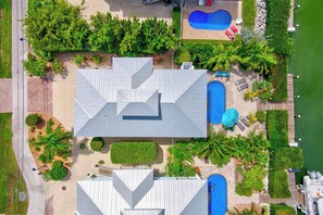 Una proprietà residenziale con una grande casa, due piscine e un giardino curato con diverse piante e un pontile.