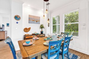 A dining area with a wooden table set for four, blue chairs, and a view of greenery through the window blinds.