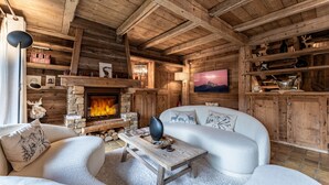 L’intérieur d’un chalet confortable, avec une cheminée, un canapé, une table basse et des étagères en bois où sont disposés divers objets.