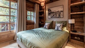 Une chambre dans une cabane en bois, avec un grand lit, une fenêtre avec des rideaux, un tableau accroché au mur et des étagères en bois.