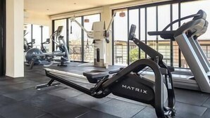 Een moderne fitnessruimte met cardiotoestellen, waaronder een loopband en hometrainers, en grote ramen met uitzicht.