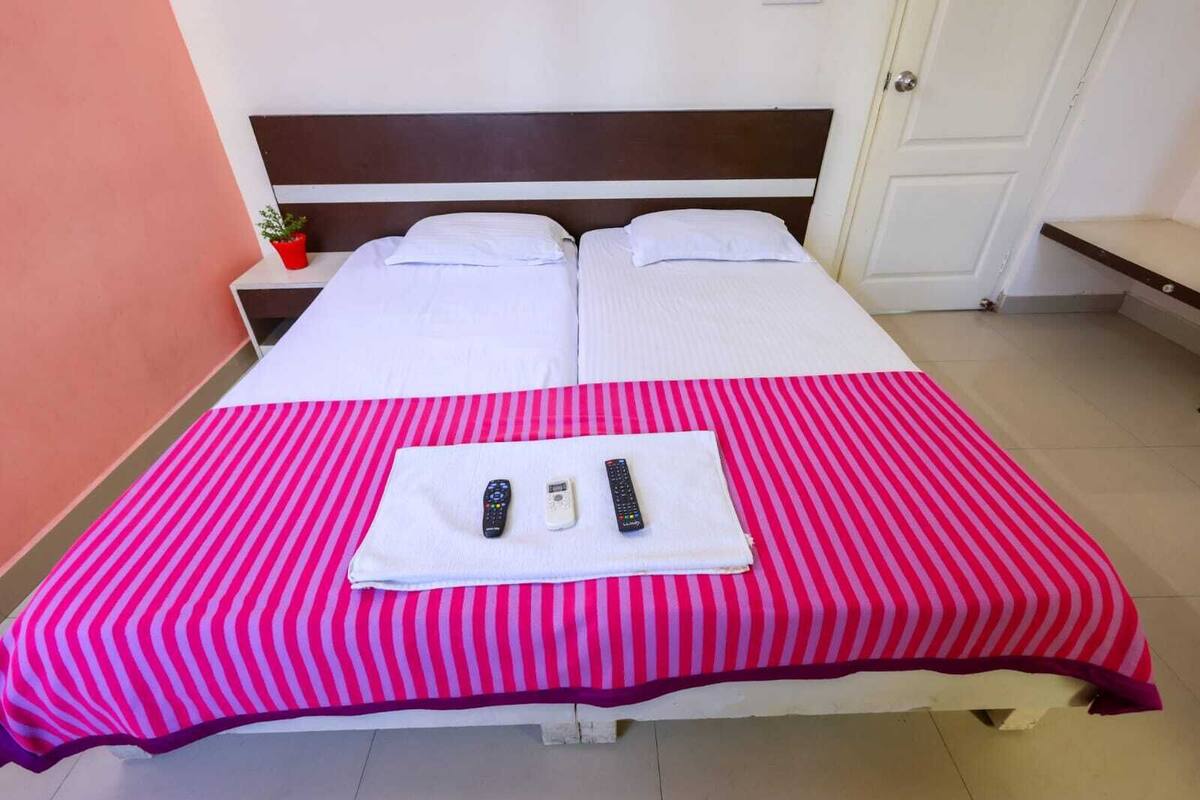 A double bed with a striped pink and white bedspread, two white pillows, and a folded towel with two remote controls on it.