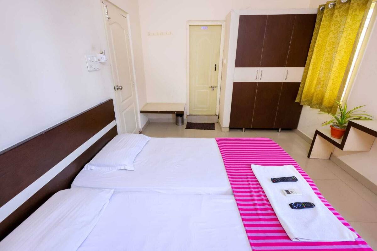 A hotel room with two beds, a wardrobe, a small table with a plant, and a bathroom door.