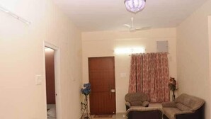 A living room with a sofa, armchair, ottoman, and a door leading to another room. - Sucasa Homes (Hyderabad)