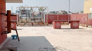 A rooftop terrace with a red wall, a blue stool, and a metal fence. - Sucasa Homes (Hyderabad)