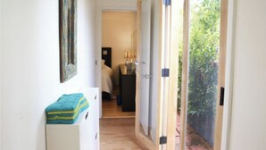 A narrow hallway with a bed, a small table with a lamp, and a door leading to a garden. - Santa Monica 3 bedroom house with sunny outdoor deck (Los Angeles)