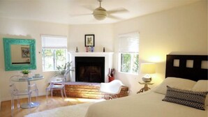 A bedroom with a fireplace, a bed with patterned pillows, a round glass table with chairs, and a ceiling fan. - Santa Monica 3 bedroom house with sunny outdoor deck (Los Angeles)