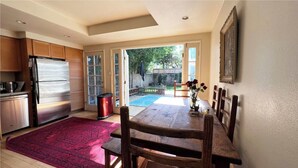 A kitchen with a stainless steel refrigerator, wooden cabinets, and a red rug. There is a dining table with chairs and a vase with flowers. - Santa Monica 3 bedroom house with sunny outdoor deck (Los Angeles)