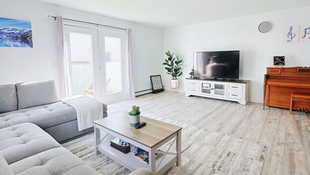 Ein modernes Wohnzimmer mit grauem Sofa, einem Holztisch, einem TV-Schrank und einer Holzkommode.